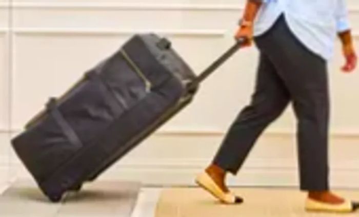 A person rolls the Mark & Graham Terminal 1 Checked Rolling Duffle Bag across rocky terrain