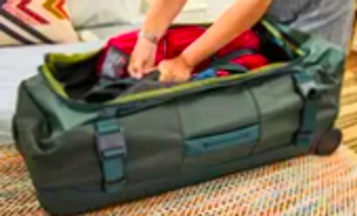 A person loads clothing into the Away The Outdoor Rolling Duffel 85L