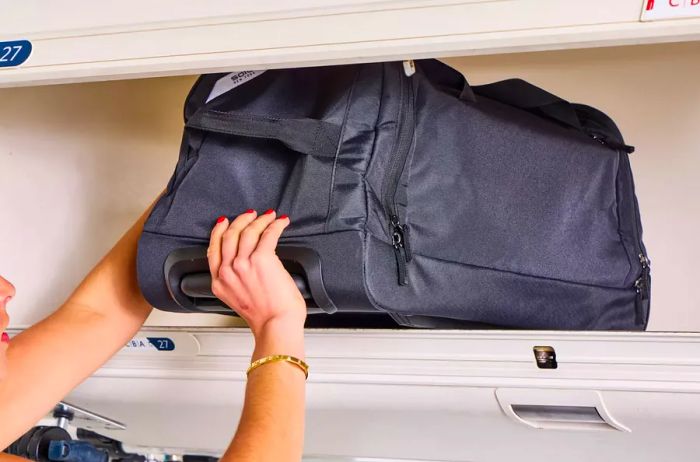 A person places the Solo Leroy Rolling Duffel into an overhead bin