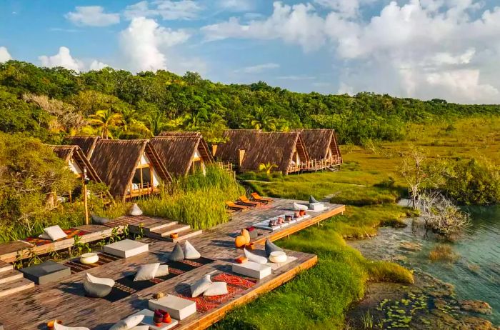 The exterior of Habitas Bacalar in Mexico, featuring lounge chairs on a wooden deck by the water