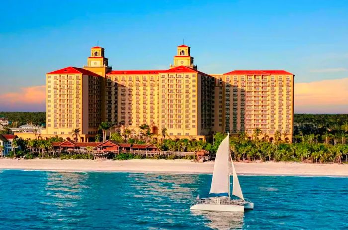 A picturesque view of The Ritz-Carlton Naples with the ocean and sandy beach in the foreground as a boat glides by