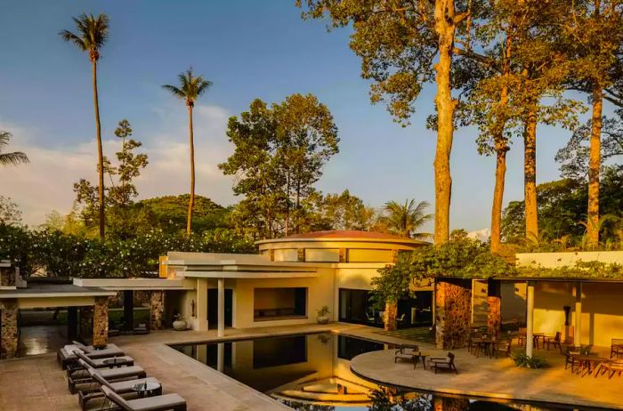 An exterior view of the main resort pool framed by towering palm trees during the golden hour at Amansara.