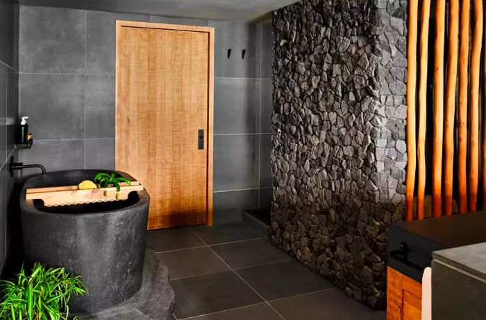 Suite bathroom showcasing a black freestanding tub and rock wall.