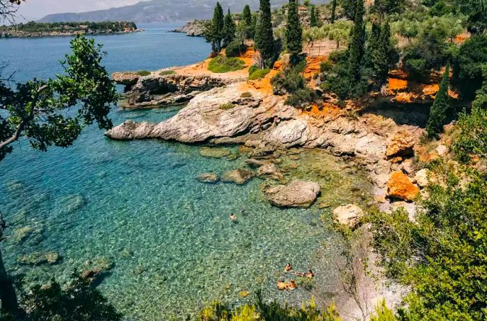 A secluded cove in Kardamyli, Greece, enveloped in lush greenery, with four people enjoying the refreshing water.