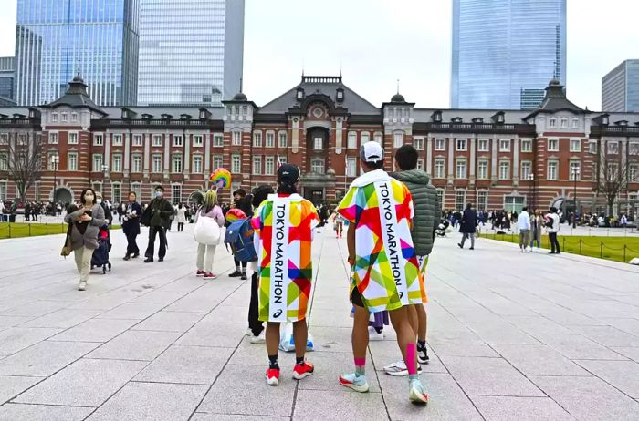 Two individuals wrapped in Tokyo Marathon blankets outside Tokyo Station.