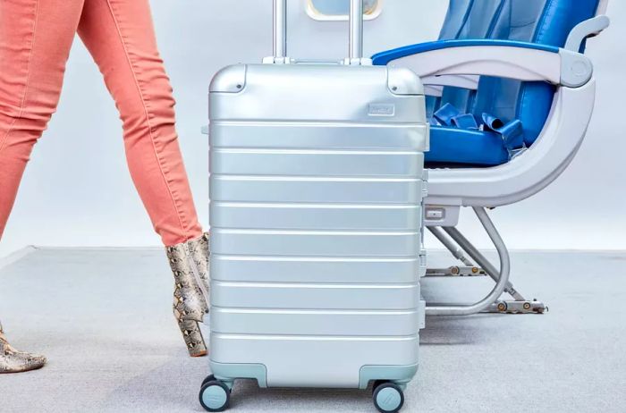 A person is maneuvering an Away The Bigger Carry-on: Aluminum Edition in an airplane environment