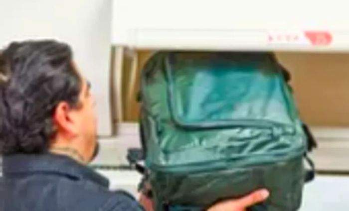 A person places the Away F.A.R. Convertible Backpack 45L in an overhead compartment.