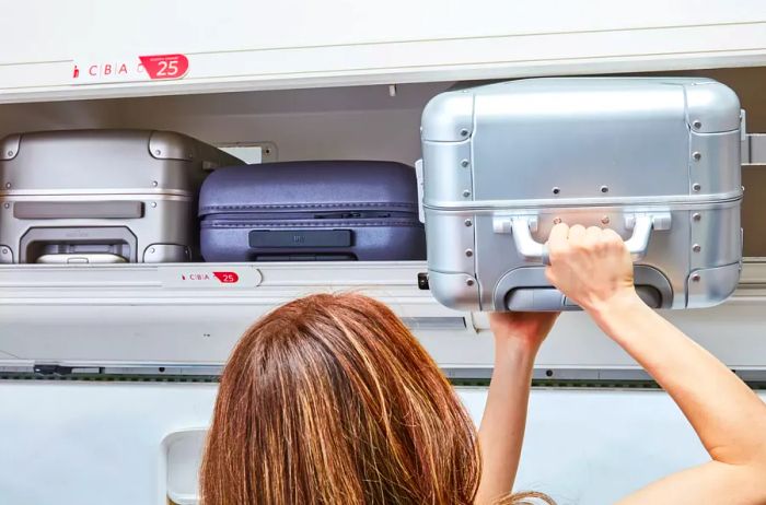 An individual places the Away The Bigger Carry-On: Aluminum Edition into an overhead compartment.