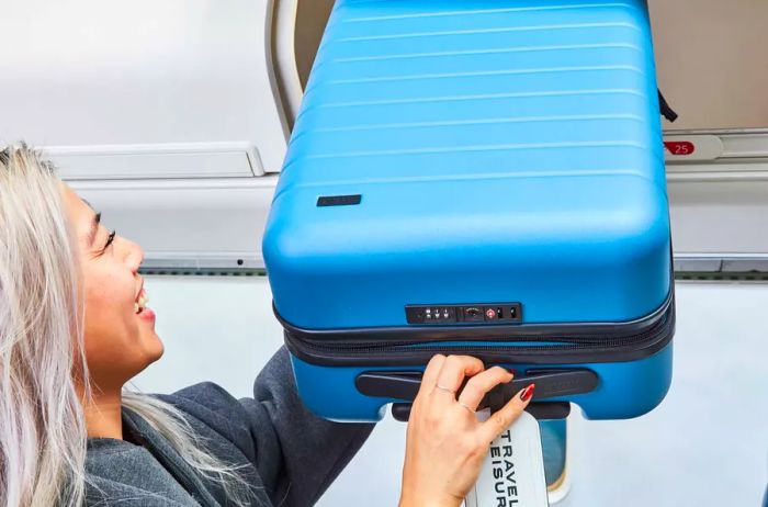 A person stowing the Away The Carry-on Flex in an airplane's overhead compartment.