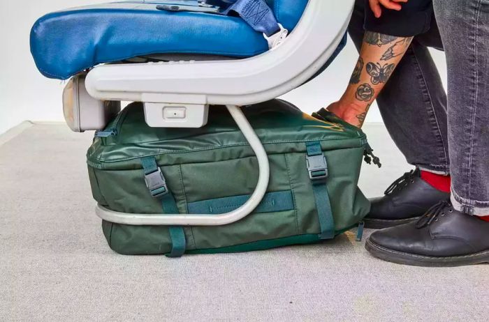 A person slides the Away F.A.R. Convertible Backpack 45L under a seat.