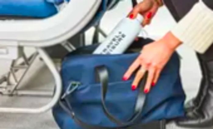 A person inserts a water bottle into the Away The Everywhere Bag.