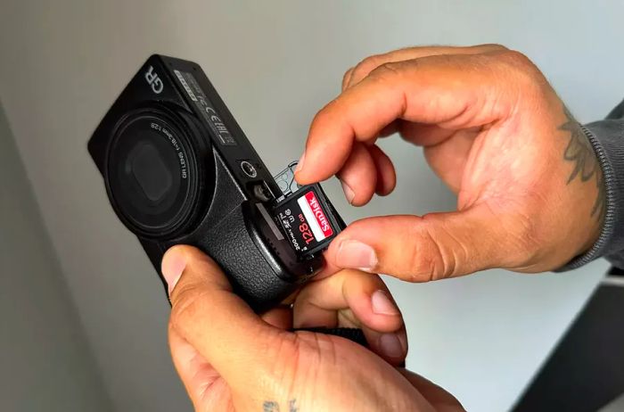 individual inserting a memory card into the Ricoh GR III Digital Camera