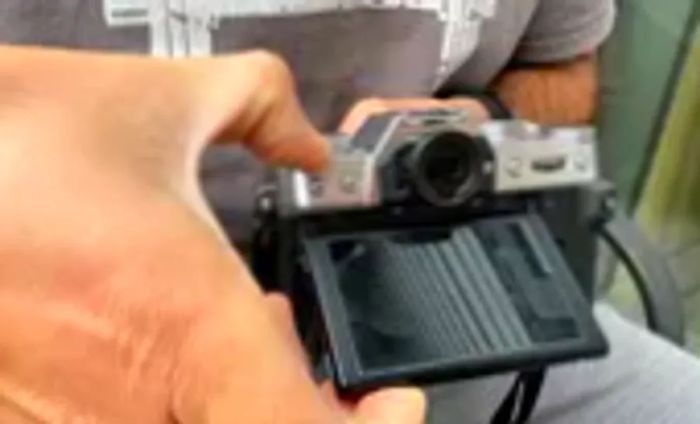 An individual is pressing a button on the Fujifilm X-T30 II while adjusting the screen