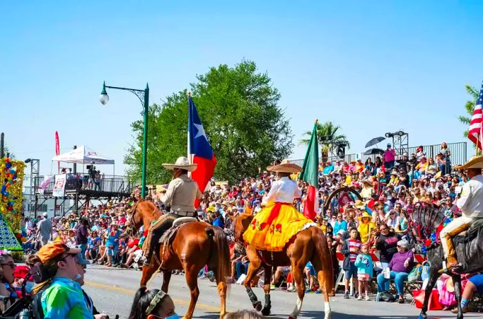 The crowd gathers for the Battle of Flowers parade alongside a group of horseback riders.