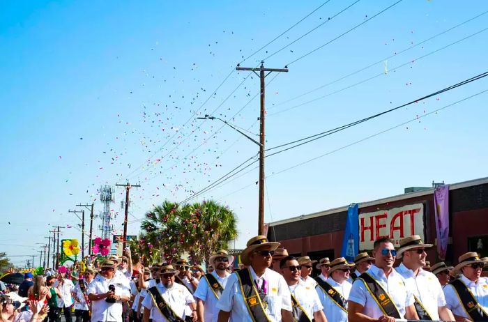 Members of the Rey Feo Consejo Education Foundation march as confetti rains down around them.