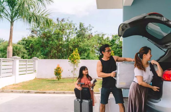 A family of Asian descent loading their bags into a vehicle, accompanied by their daughter