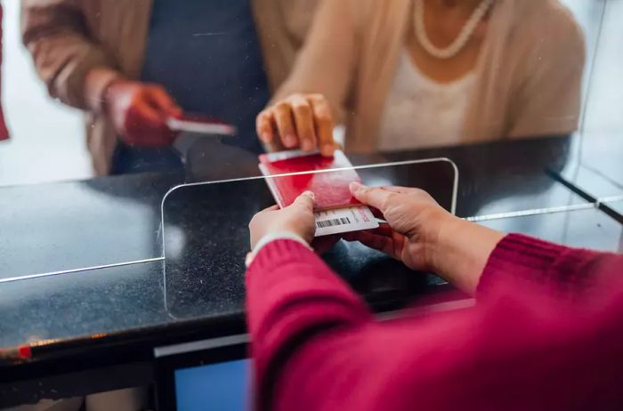 A female passenger assistant handing a passenger's boarding pass and passport at the airline check-in desk in an international airport.