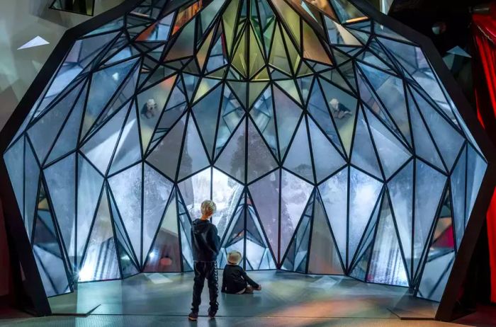 Children standing before a mirrored surface that refracts light in a museum