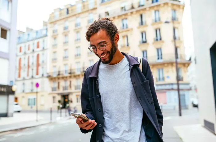 Contemporary young man with curly hair exploring the city while checking his smartphone.