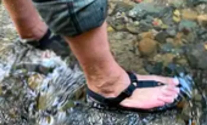 A person stands in a stream while wearing Bedrock Cairn Adventure Sandals