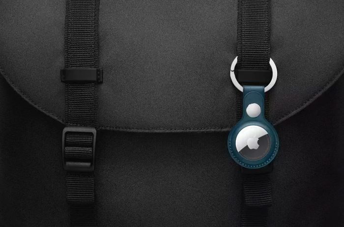 A close-up shot of an AirTag keychain attached to a sleek black backpack