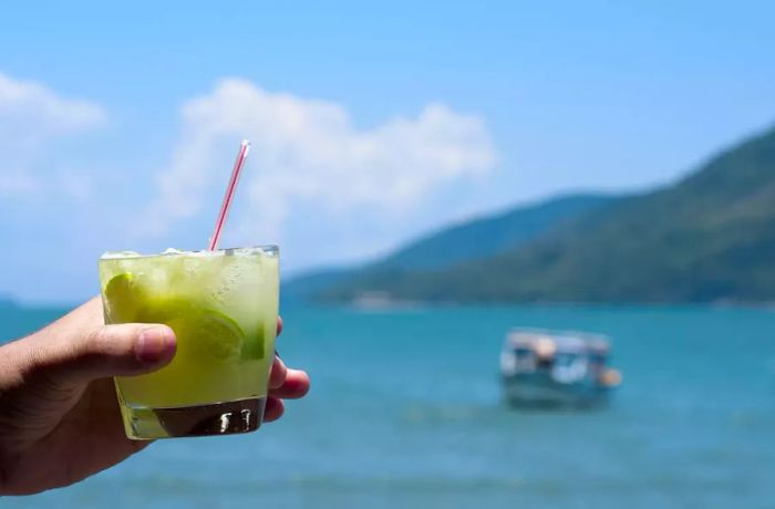 A hand enjoying a caipirinha on the beach in Paraty, RJ, Brazil - stock photo