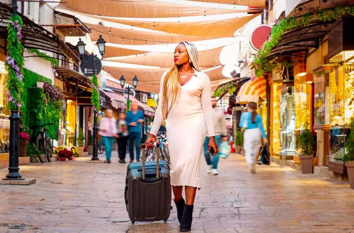 A Black woman traveling with a suitcase along a European street