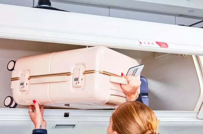 Hands placing the July Carry On Trunk into the overhead compartment of an airplane