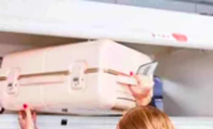 Hands lifting the July Carry On Trunk into the overhead compartment of an airplane