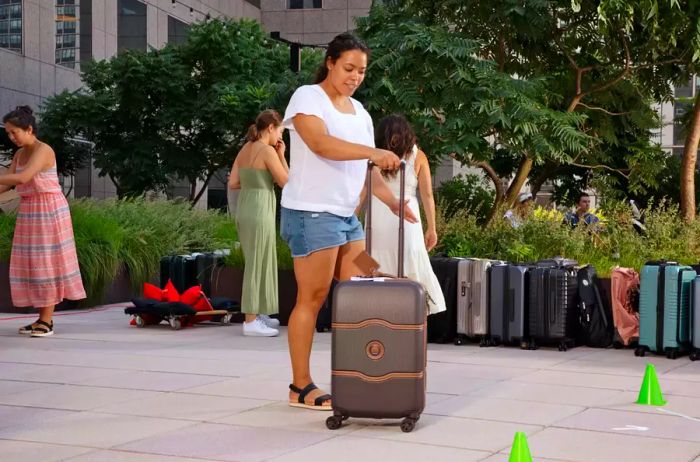 A woman rolls a piece of Delsey Paris luggage along a sidewalk.