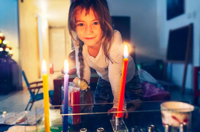 A young girl lighting a menorah at home.