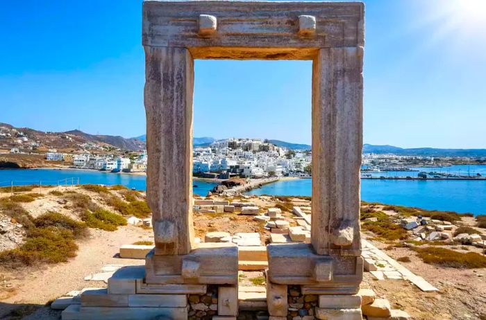 A view through the iconic Portara marble gateway on Naxos island towards the city and harbor in the Cyclades, Greece.