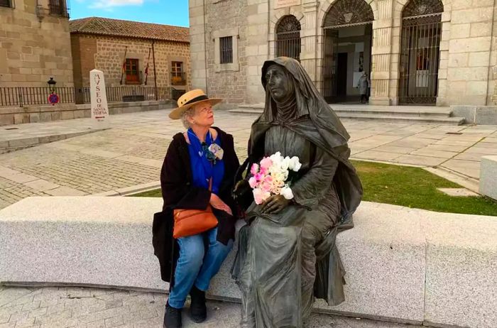 A mature woman sitting alongside Santa Teresa at the Convent of Santa Teresa in Avila, Spain