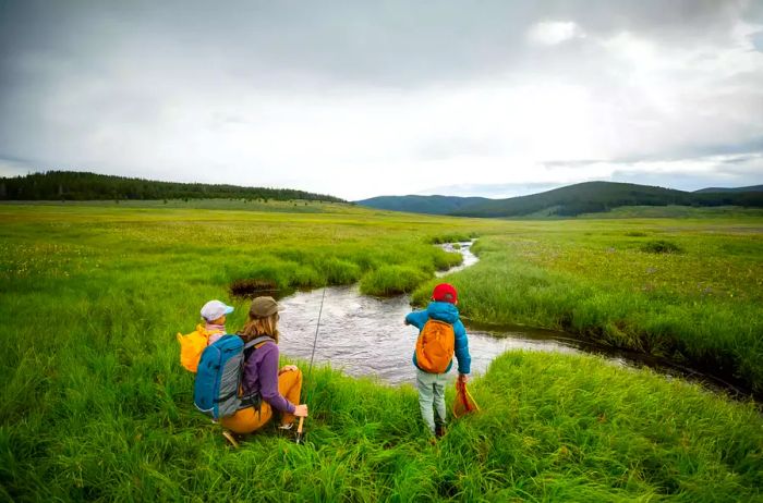 A mother and her two children enjoy fishing in a picturesque creek setting.