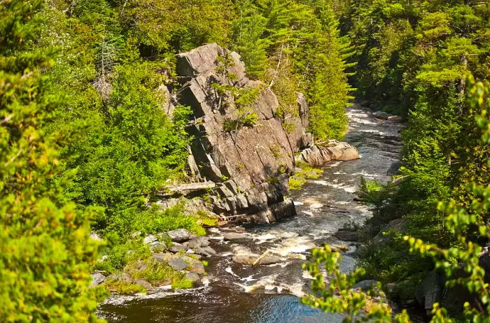 The Pleasant River cascades dramatically through a gorge filled with rocks, forming a beautiful waterfall.