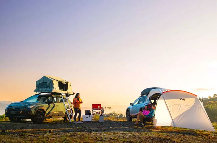 Friends with parked Subarus and camping gear