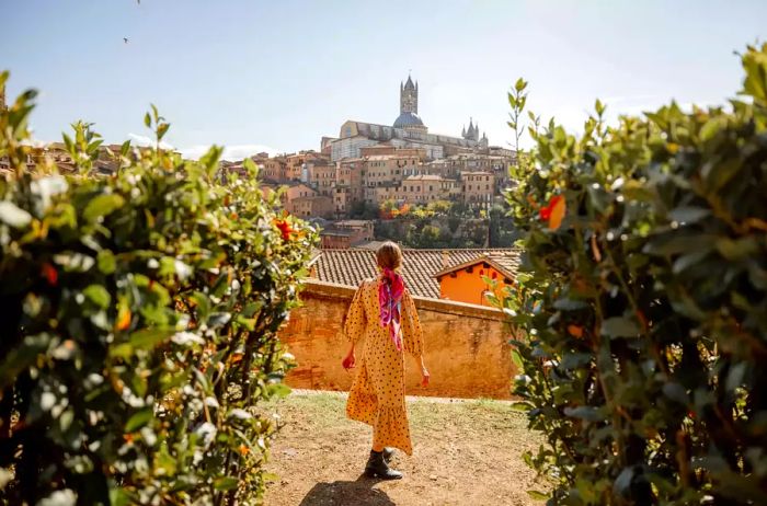 A woman strolls along a path with a view of Siena, Italy in the background