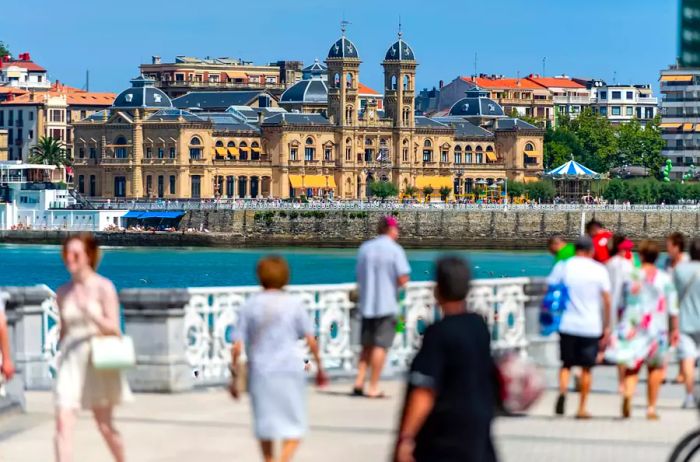 The picturesque promenade of San Sebastián, featuring the city hall, with pedestrians enjoying the scene in the foreground.