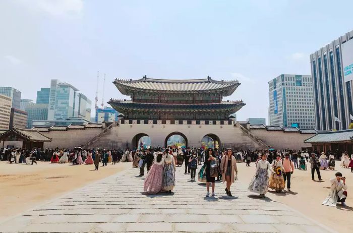 Individuals strolling in traditional Hanboks at a plaza in Seoul.