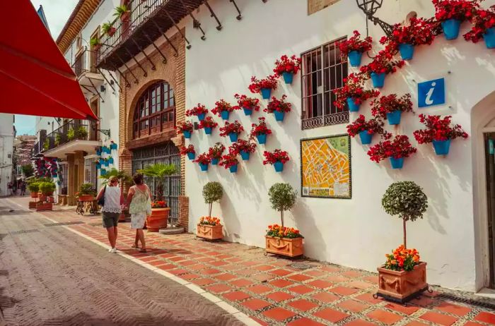 A pair of women stroll through a lively plaza in Marbella.