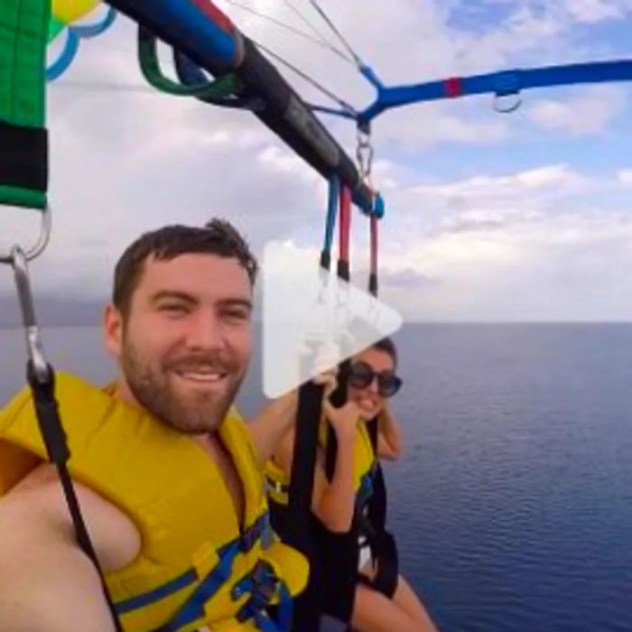 A man and woman soaring above the ocean while parasailing during a Dinogo excursion; check out the link to the YouTube video.