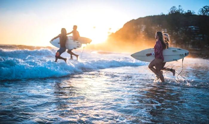 Young friends running into the ocean with surfboards