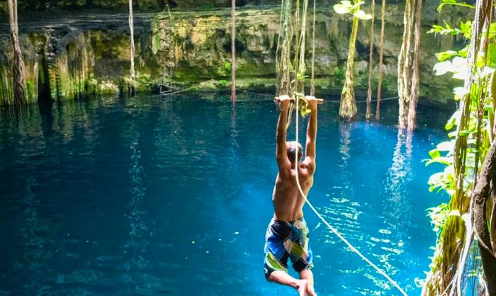 A young man leaping into a cenote in Mexico with a rope swing