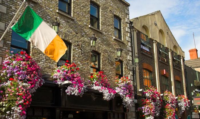 A quaint stone pub in Dublin, Ireland, adorned with an Irish flag and blooming flowers.