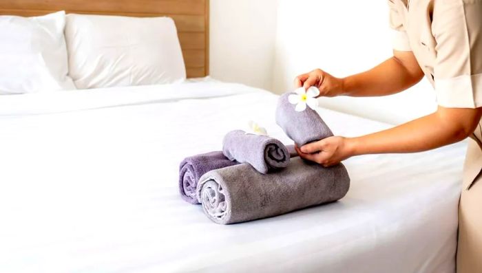 A hotel staff member gracefully arranging a plumeria flower and towels on the bed in a luxurious hotel room, preparing for incoming guests.