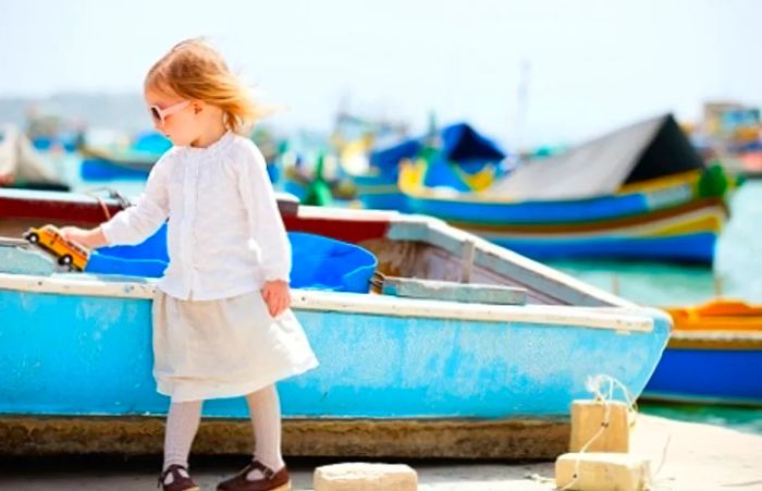 young girl playing with a Maltese toy bus at a Maltese harbor