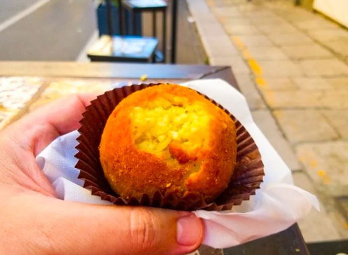 A tourist enjoying a bite of arancine on the streets