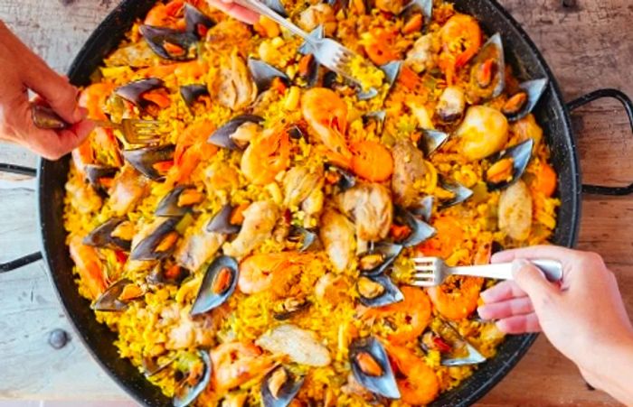 three individuals enjoying a communal dish of paella