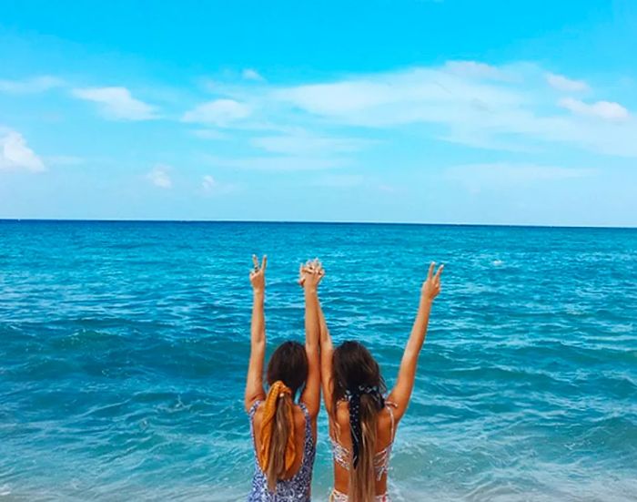 Tess and Sarah flash peace signs against the backdrop of the ocean.