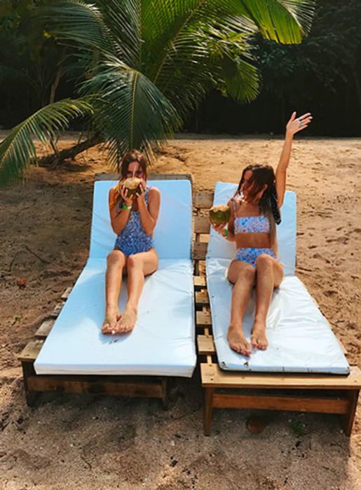 Tess and Sarah relax on lounge chairs, enjoying coconuts.